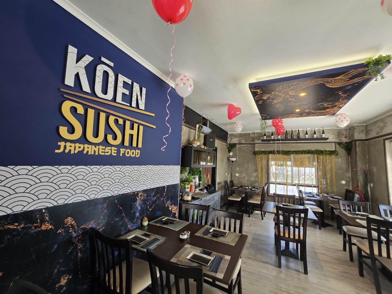 Parede azul com o logótipo Koen Sushi Japanese Food e mesas do restaurante em Massamá